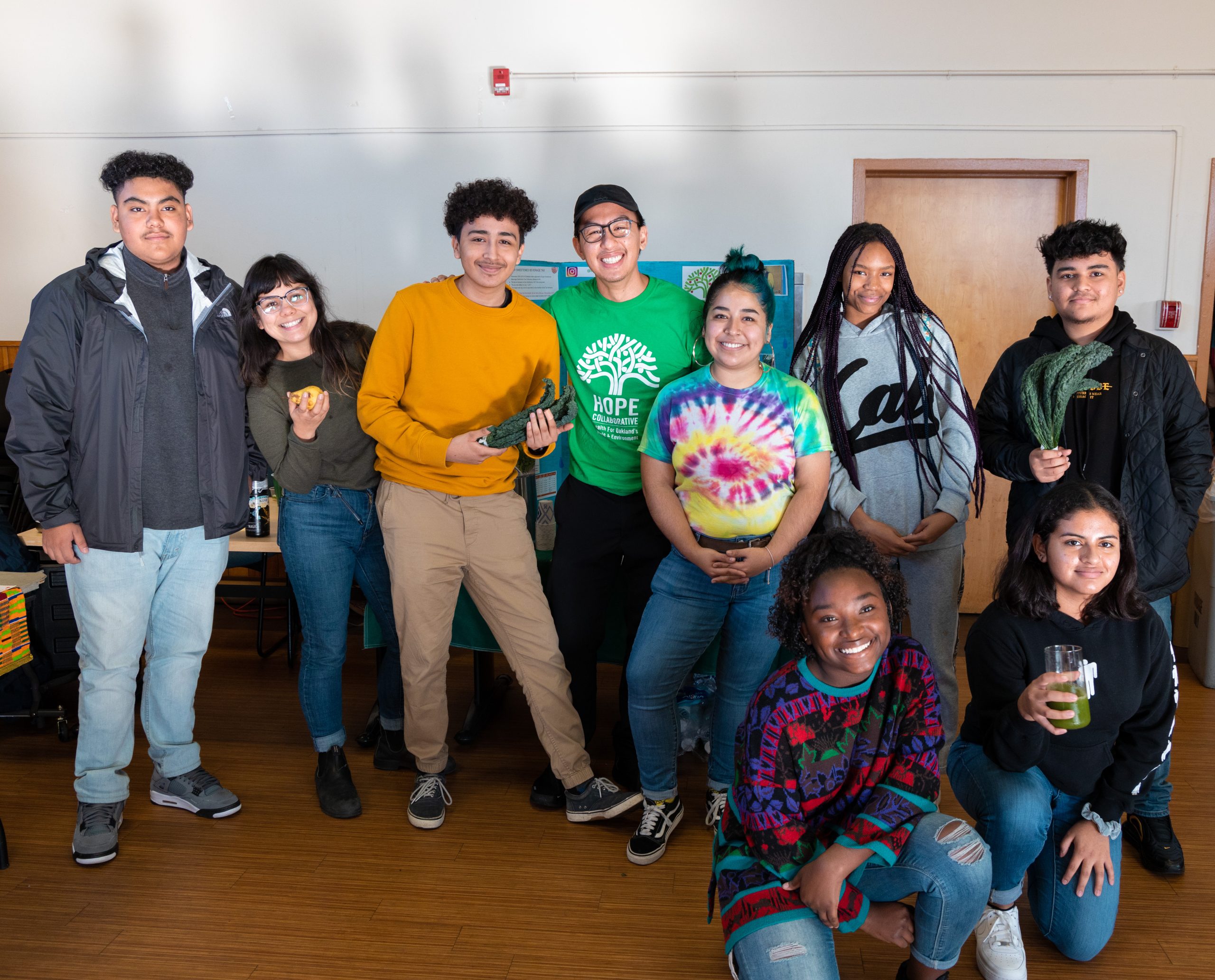 A group of youth and young adults smile. In the middle is a Southeast Asian American man who is serving fresh fresca to everyone.