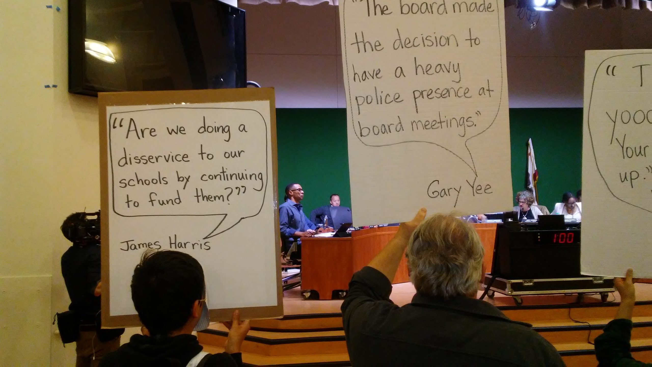 At last week's Oakland School Board meeting, Board member James Harris, one of four incumbents who will not run for re-election this year, listens to District Finance staff present their recommendations for over $20 million in budget cuts for next year. Oakland Not For Sale Protesters, holding signs in the foreground, changed their tactics, remaining silent so that the Board could not use them as an excuse to conduct public business in private.