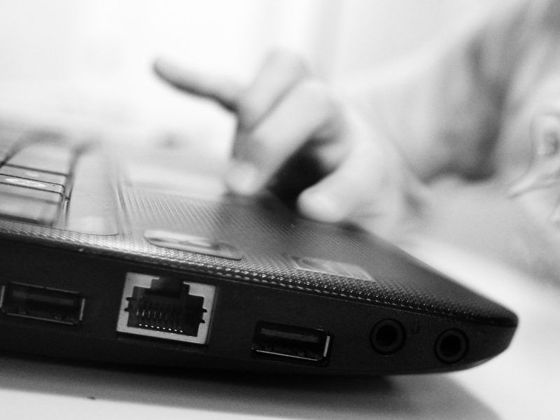 A close up black and white photo of a child's hand on the mousepad of a laptop.