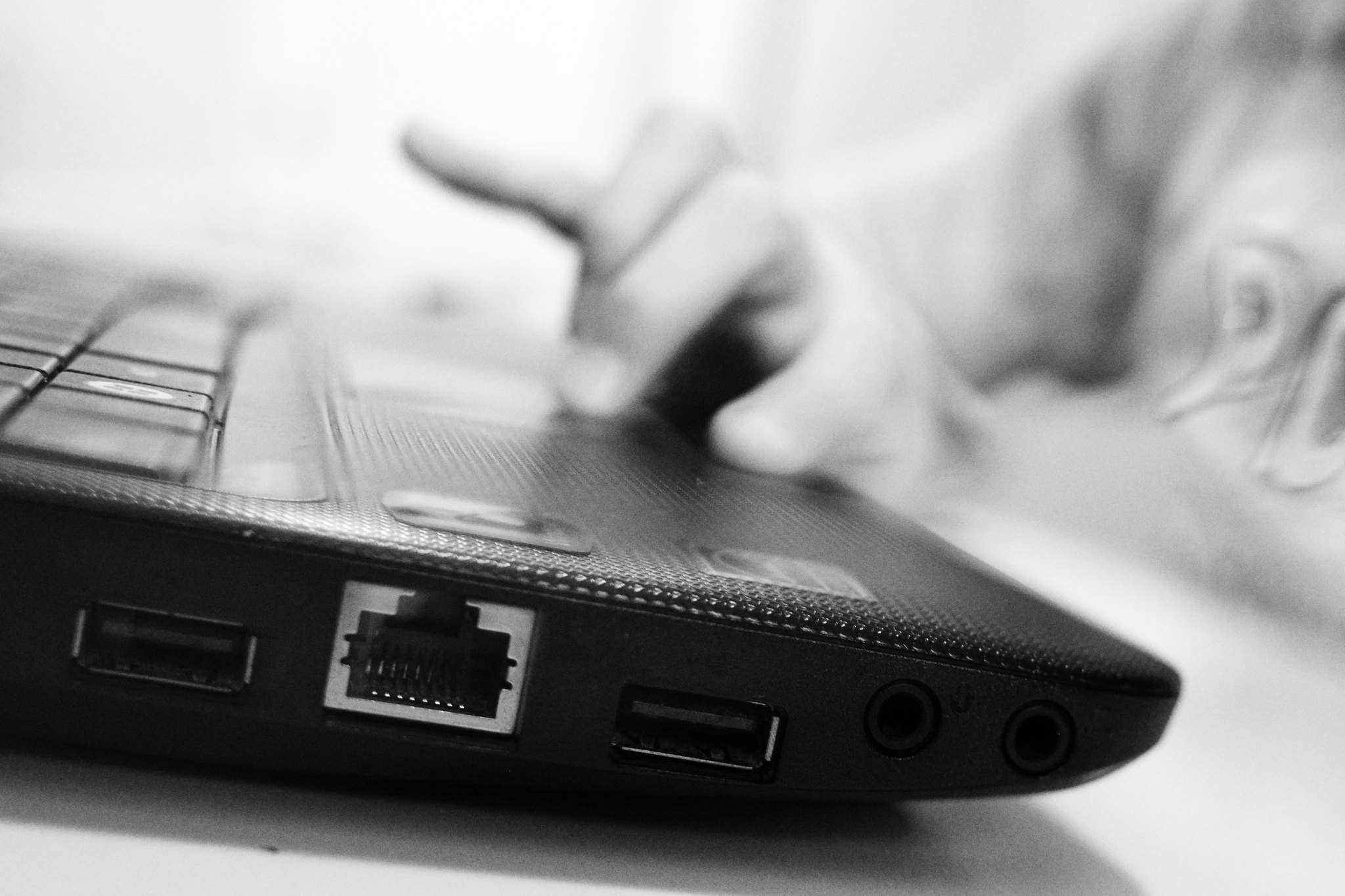 A close up black and white photo of a child's hand on the mousepad of a laptop.