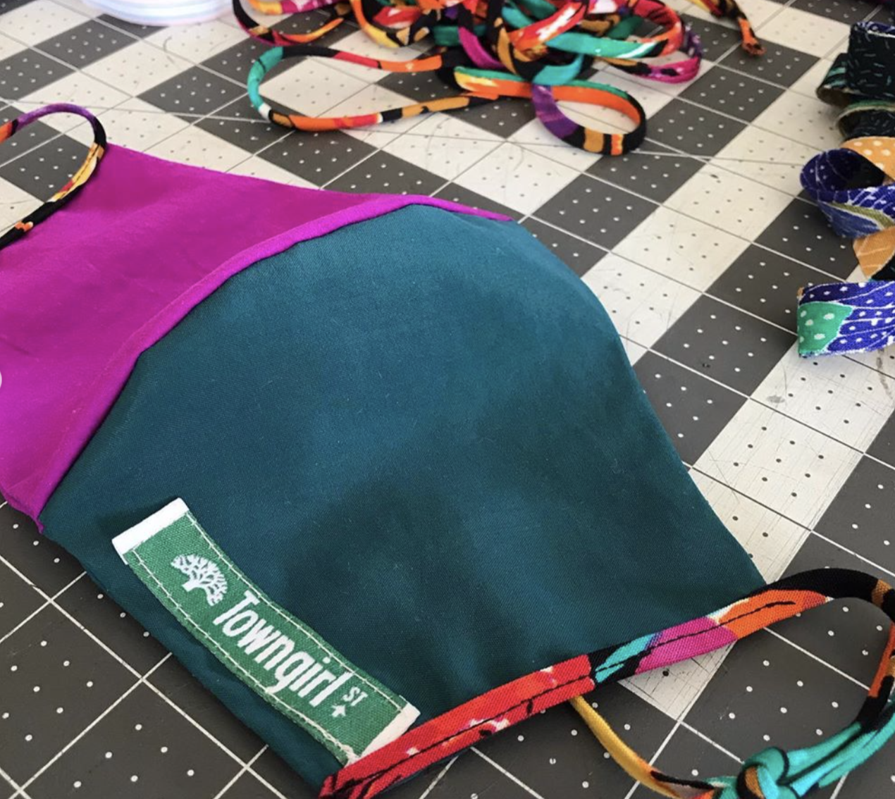 An image of a fabric face mask in fuchsia and green with "Town Girl" on the label.
