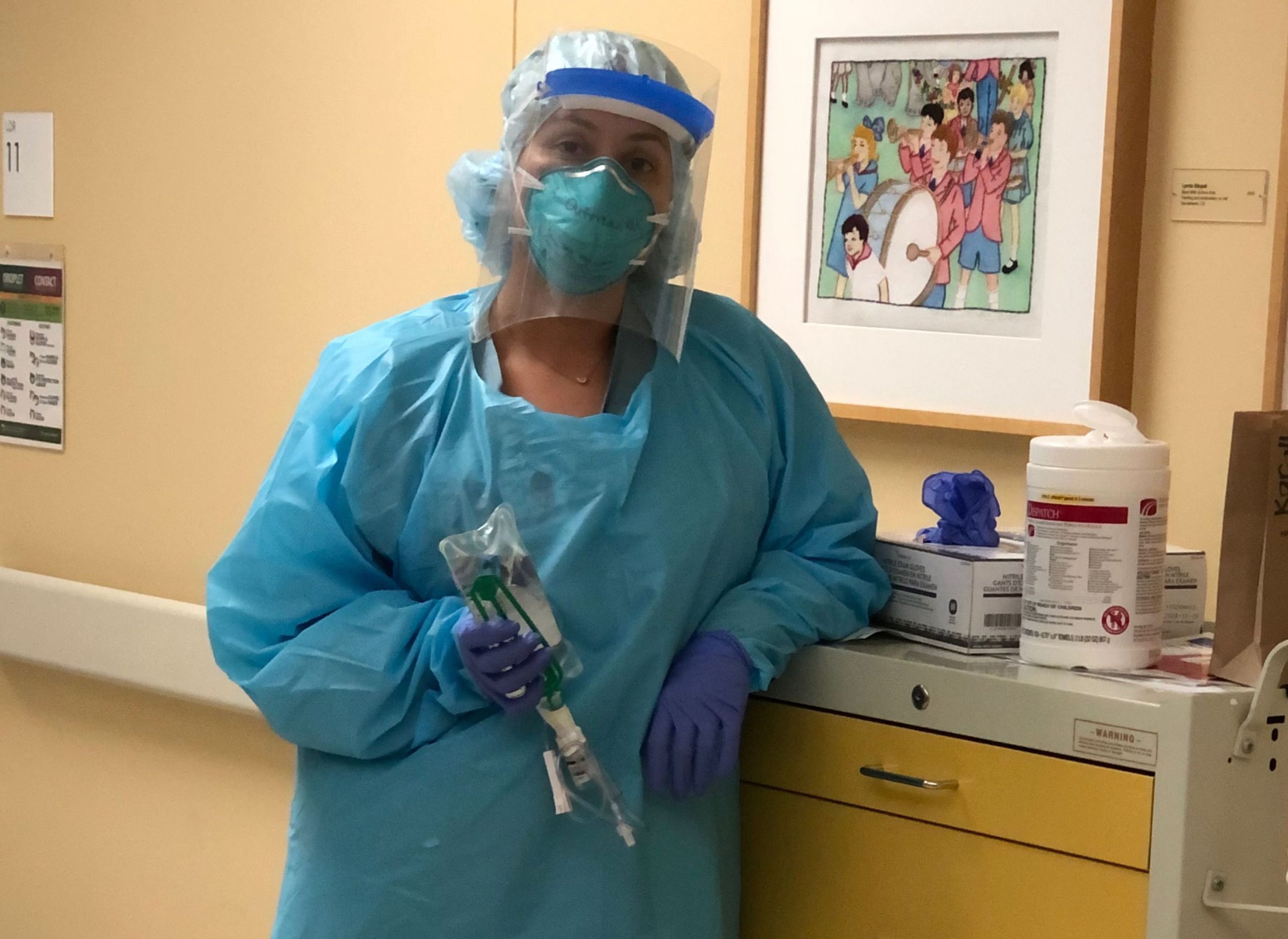 A nurse wearing full protective gear in blue at Kaiser hospital. She is wearing a plastic faceshield.