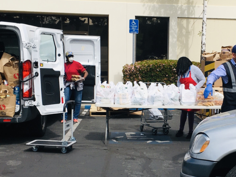 Plastic bags line a portable table in a parking lot, ready to be picked up via drive through at Arsola Food Pantry.