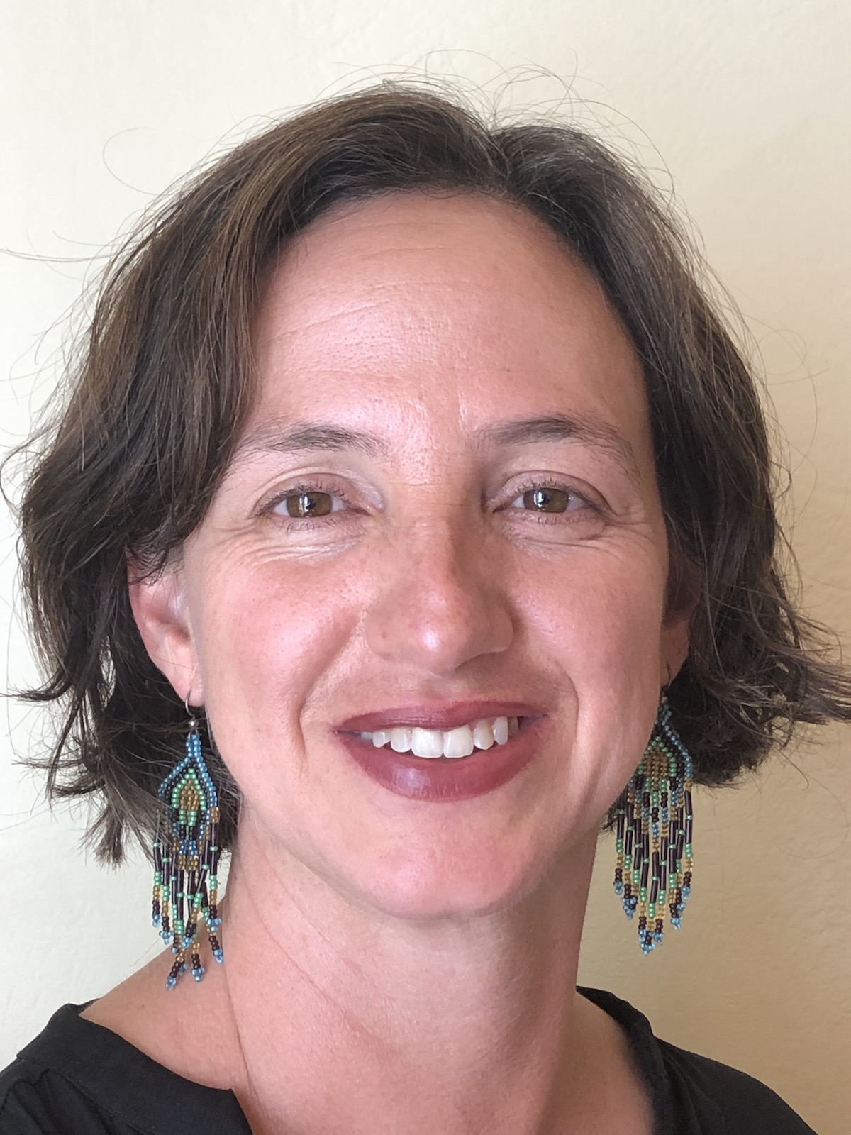 A portrait of a smiling woman with colorful earrings and a bob haircut.