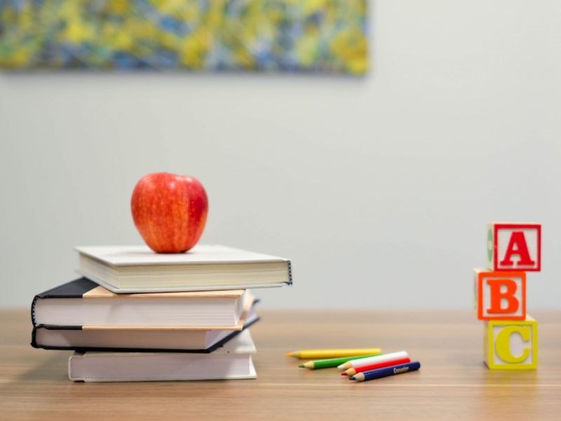 An image of a desk with a few books, an apple, and ABC blocks