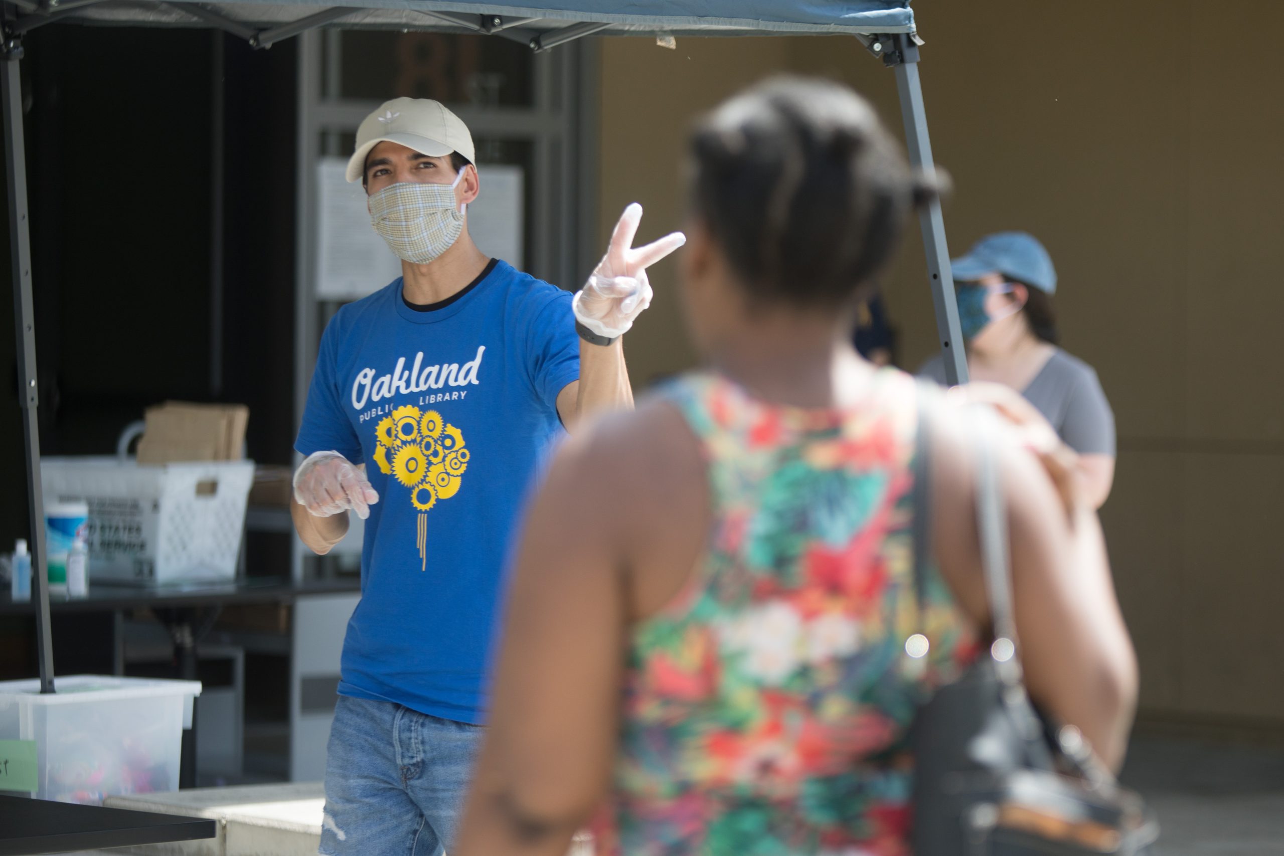 A man wearing a mask holds up the peace sign as he's handing out food bags from a library branch in East Oakland.