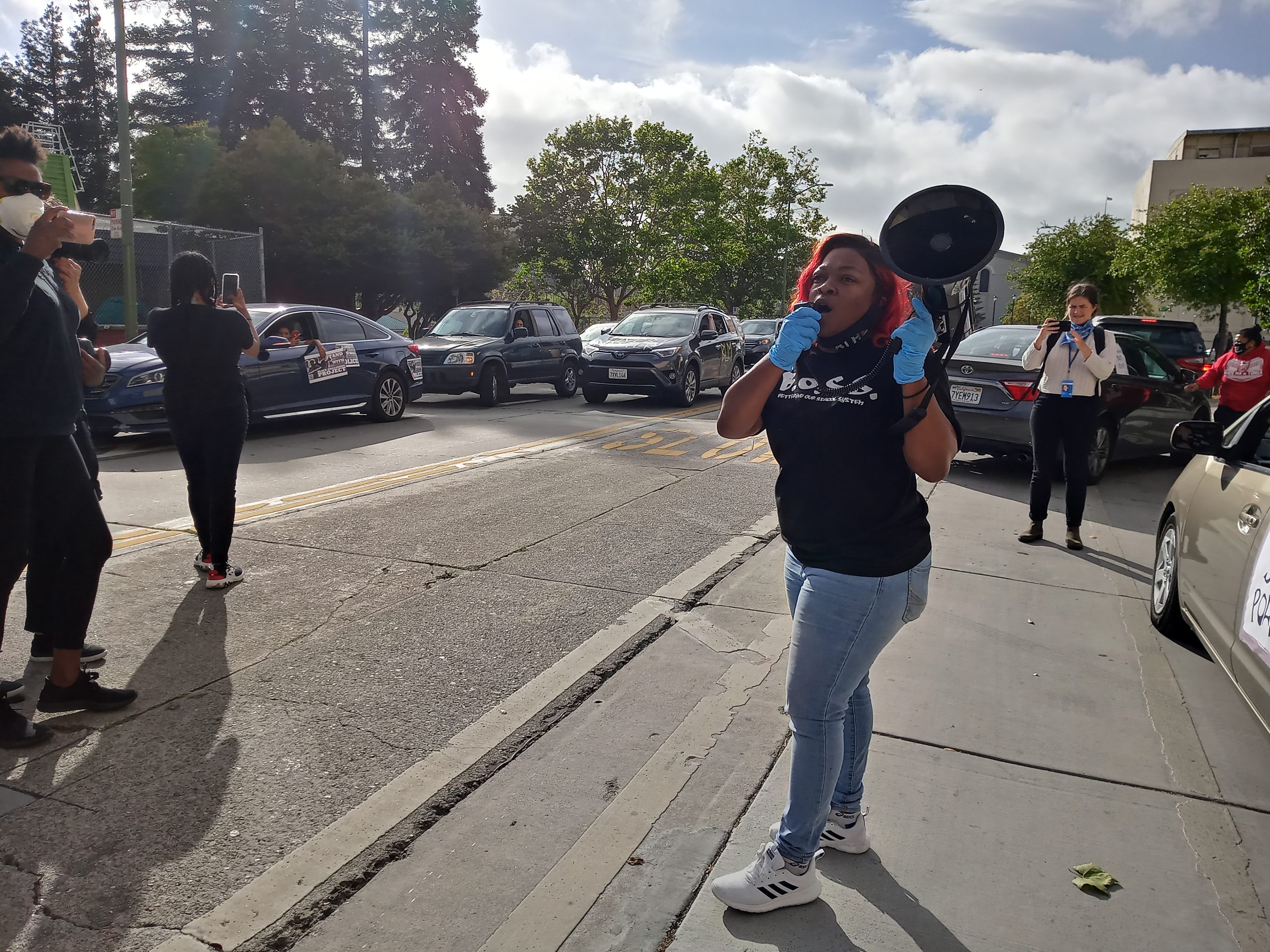 An image of an African American woman speaking into a megaphone from a sidewalk