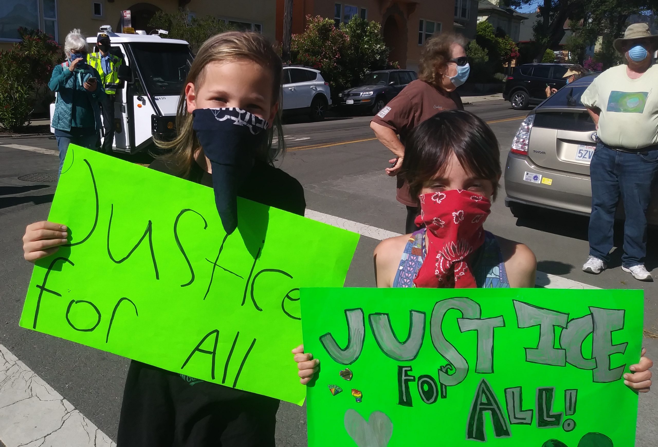 Two children wearing masks hold up handmade signs that say "justice for all."