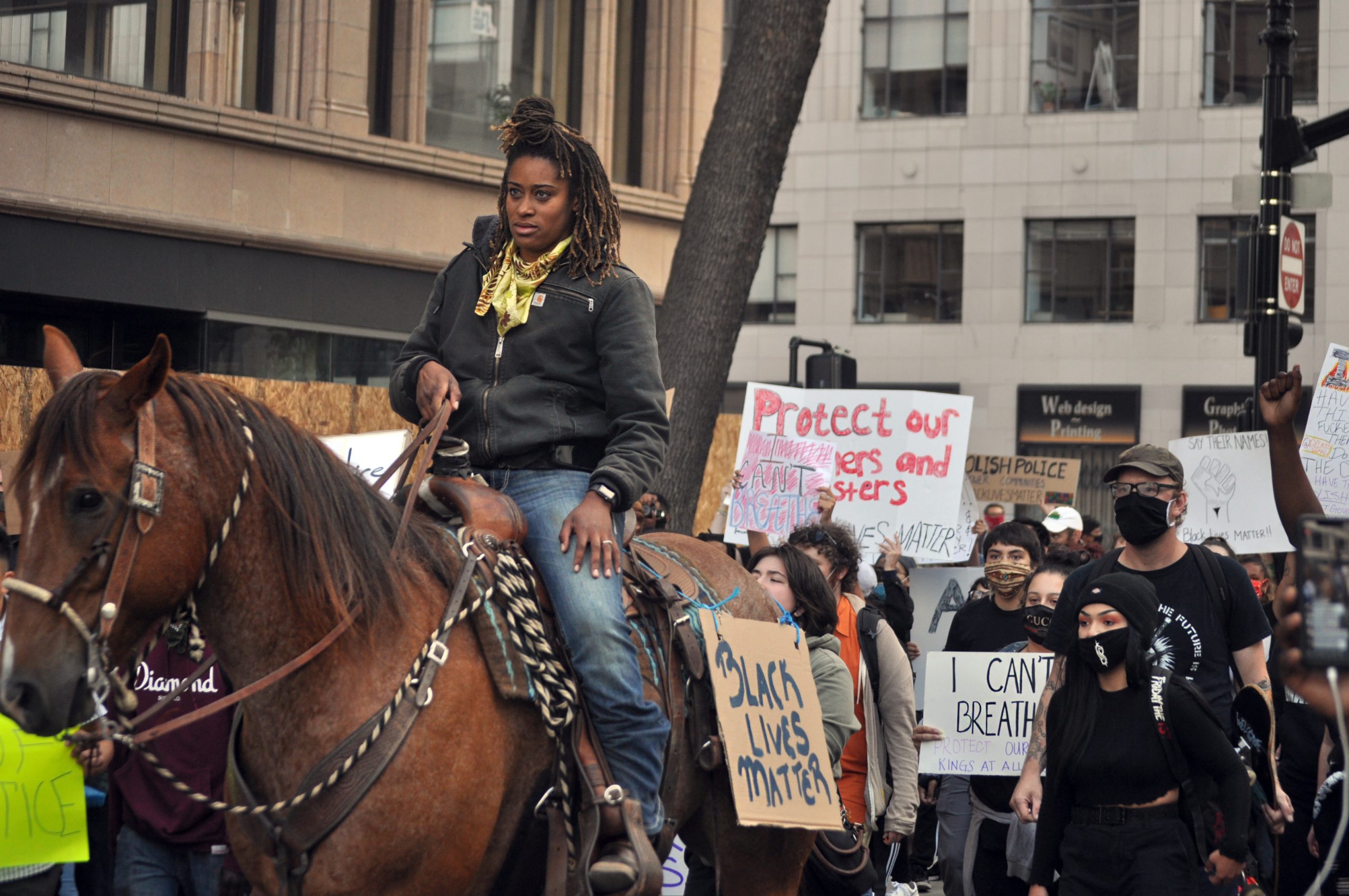 An African American woman on a horse leads a part of the protest against police brutality. A sign that says "Black Lives Matter" is on the side of her horse.