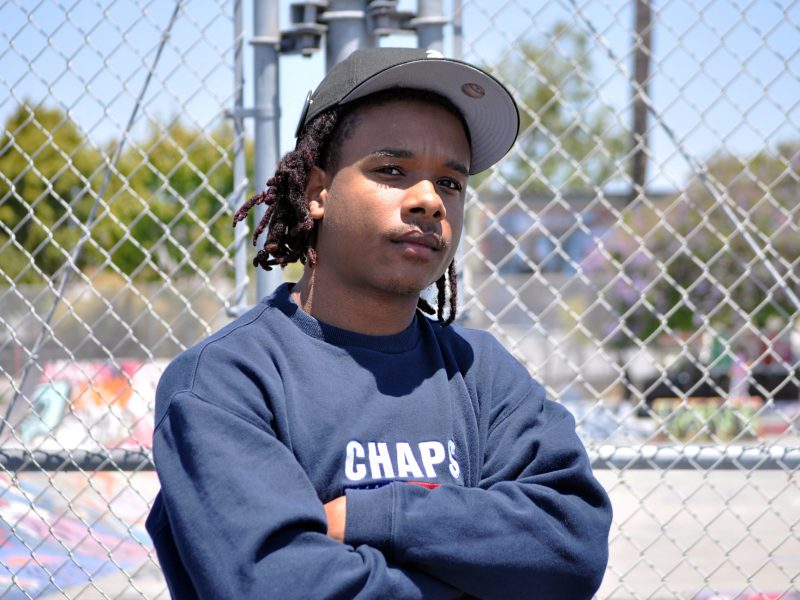A young African American man, Akil Riley, stands in front of a fence for a photo.