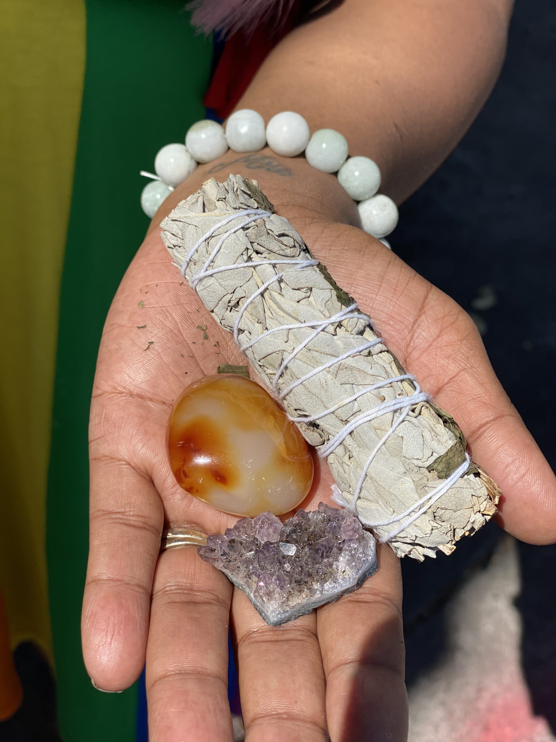 An image of a hand holding sage and crystals