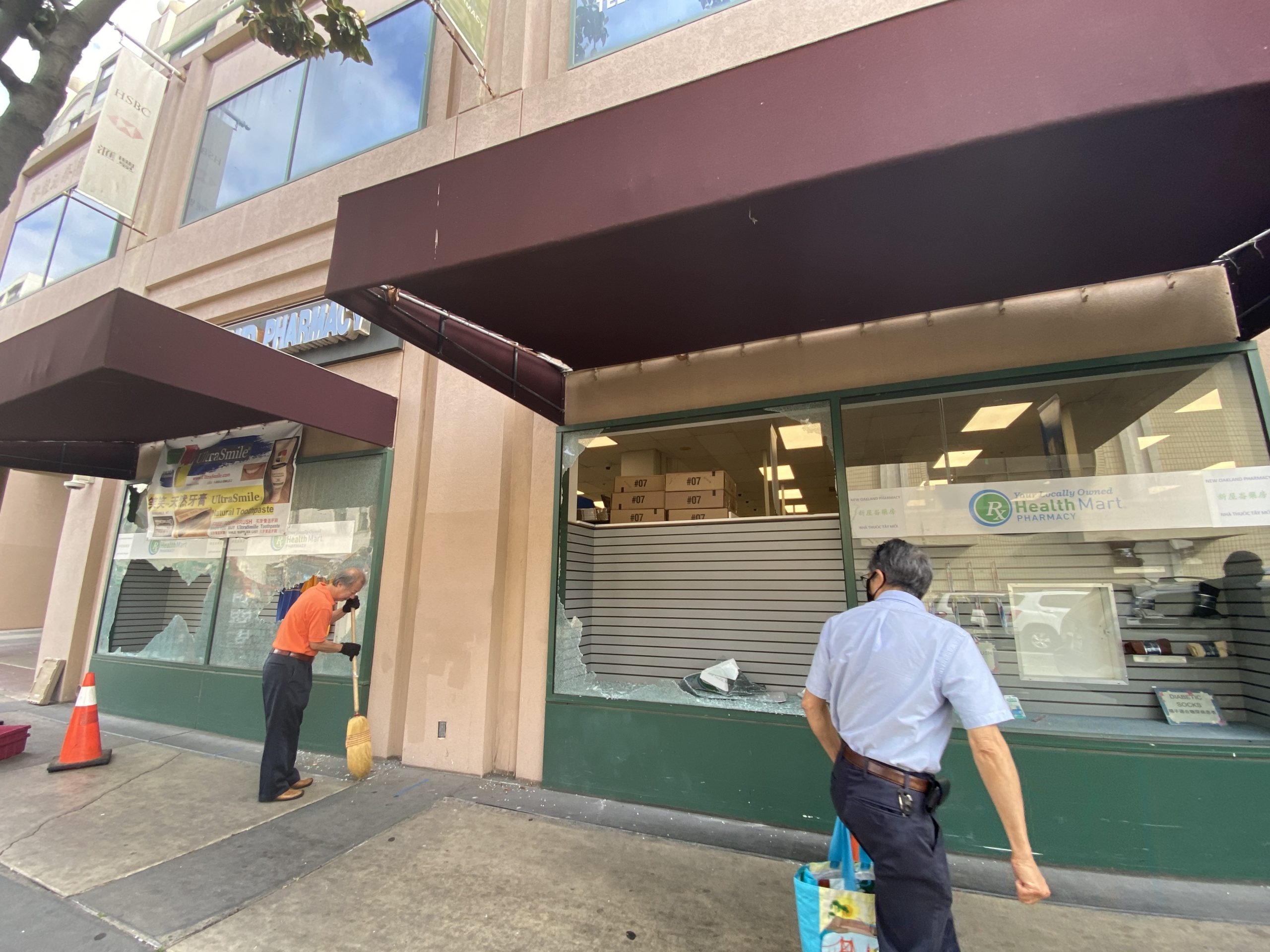 An image of a large window that is broken in Chinatown, with the owner sweeping up glass in the morning.