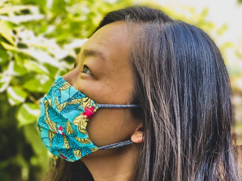 An Asian American woman poses for a profile photo wearing a colorful green mask.