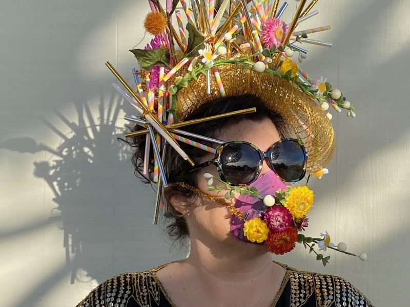 A woman wears a handmade crown made from flowers, and a mask that matches.