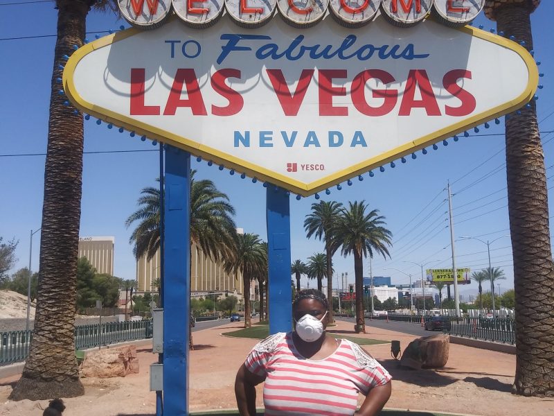 An African American woman stands in front of the Las Vegas sign, with a child running in the background