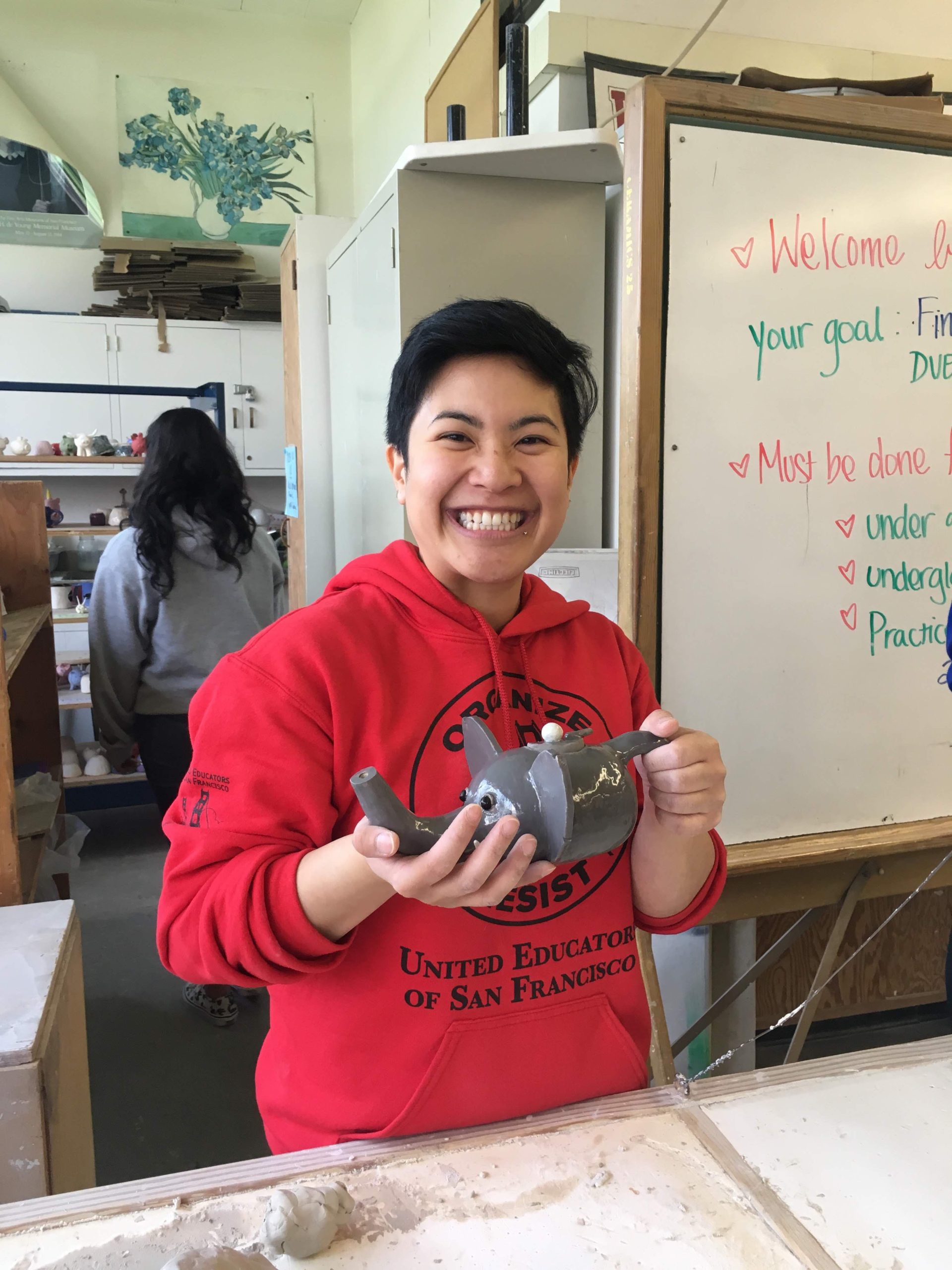 An Asian woman with short hair is holding a ceramic sculpture and smiling.