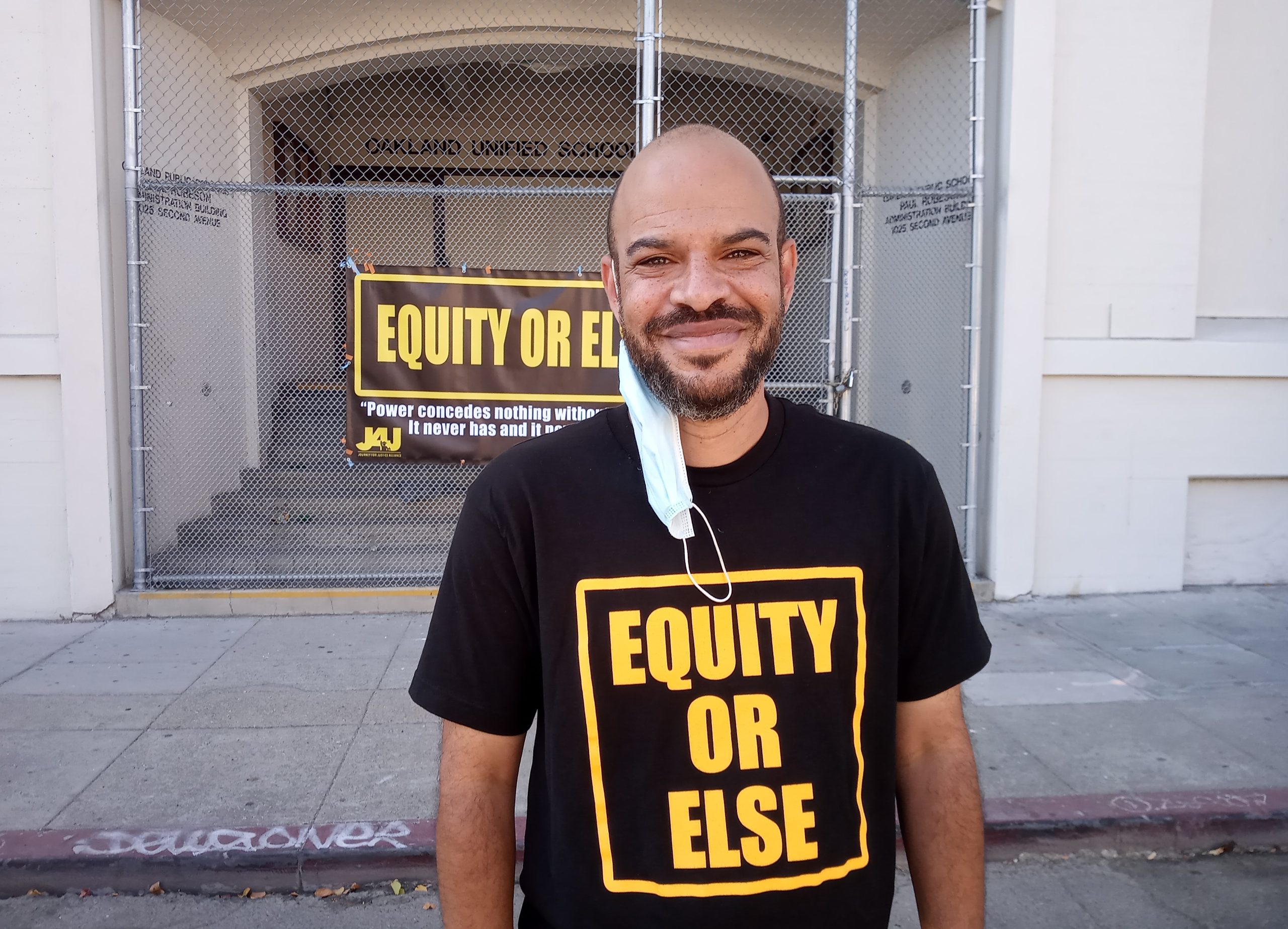 An African American man smiles for the camera in front of a school administration building.