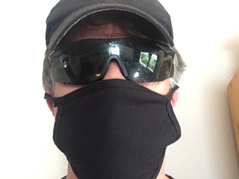 A man wears a cap, glasses, and a black mask