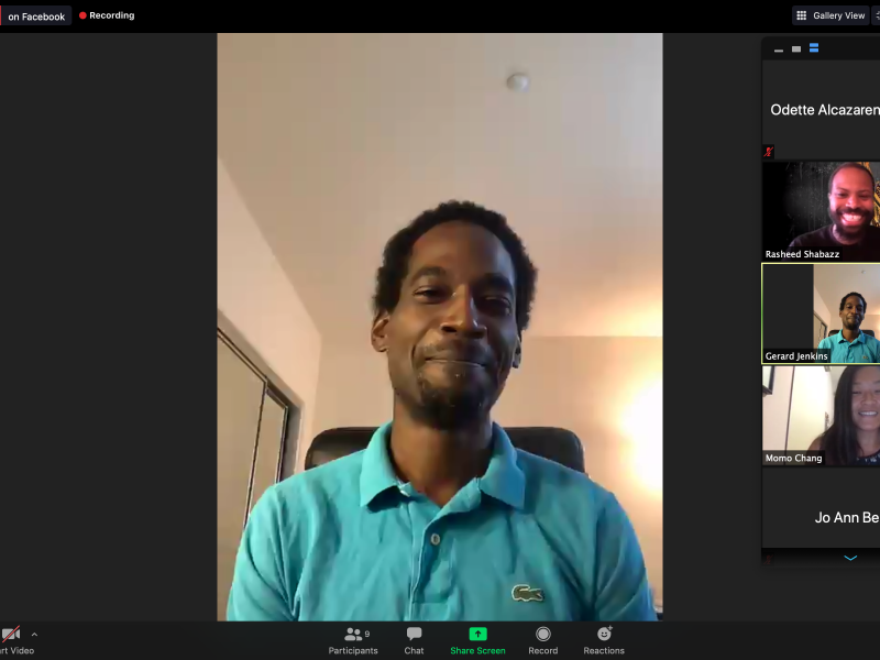 An African American man wearing a turquoise shirt speaks on a Zoom presentation.