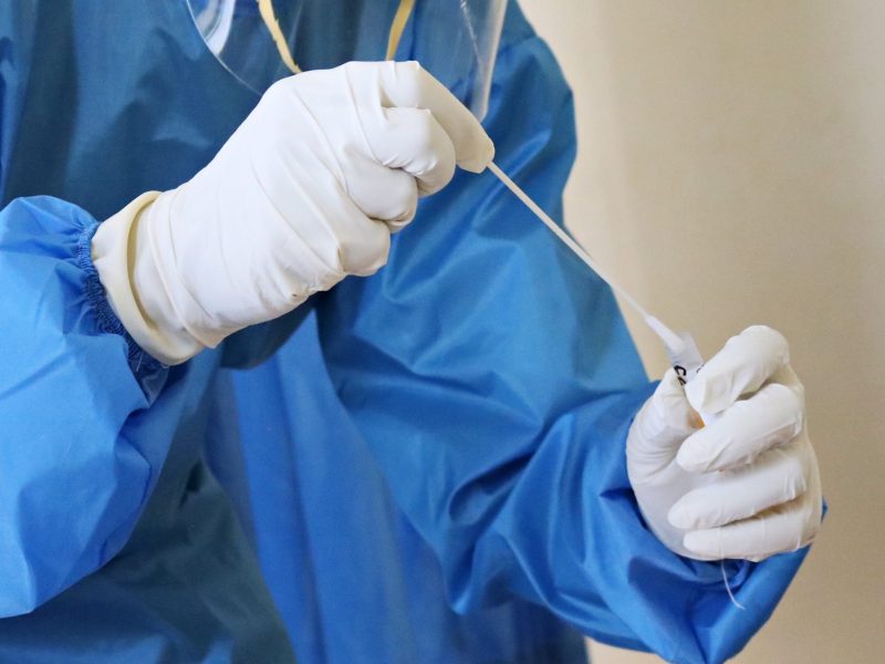 A close up of a person wearing PPEE and holding a COVID test swab