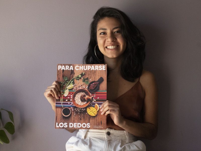 A smiling Latinx woman holds up a cookbook.