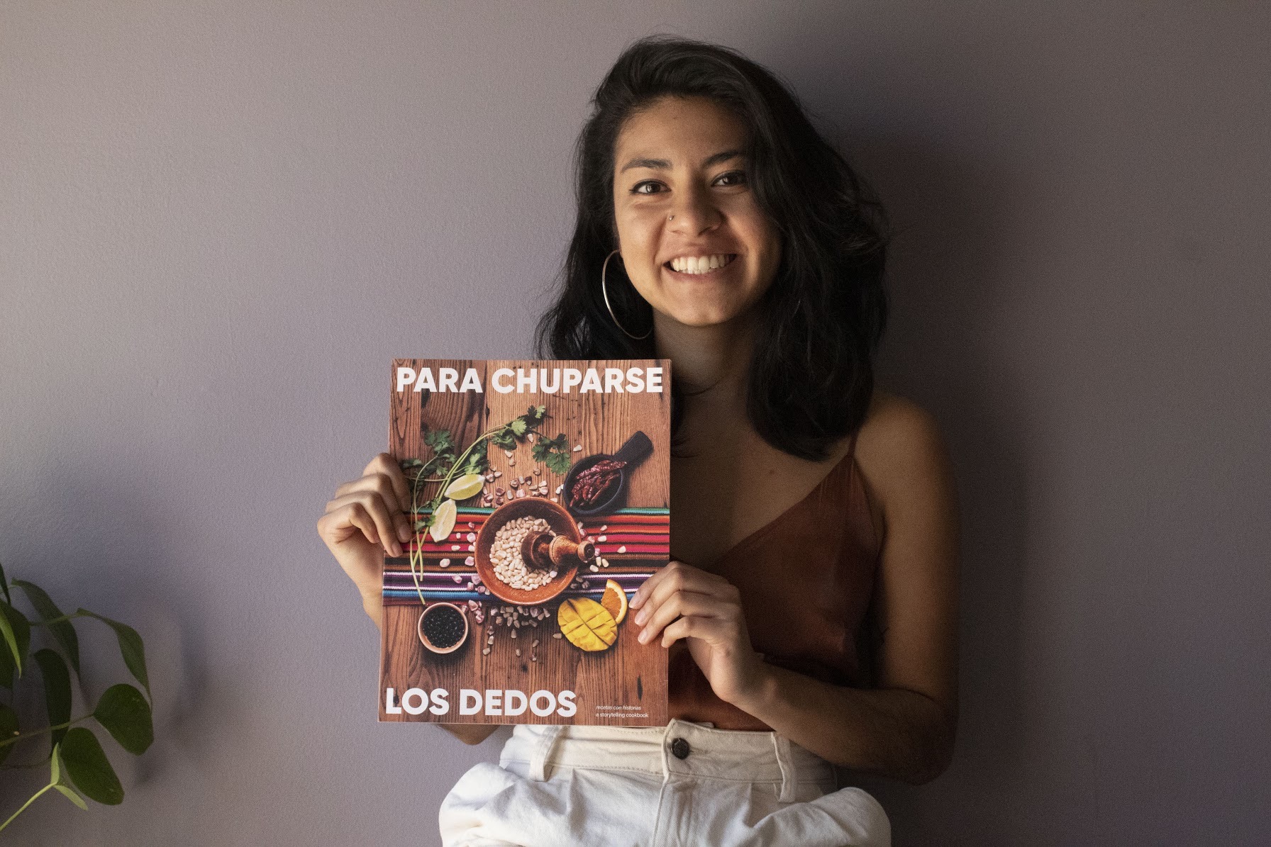 A smiling Latinx woman holds up a cookbook.