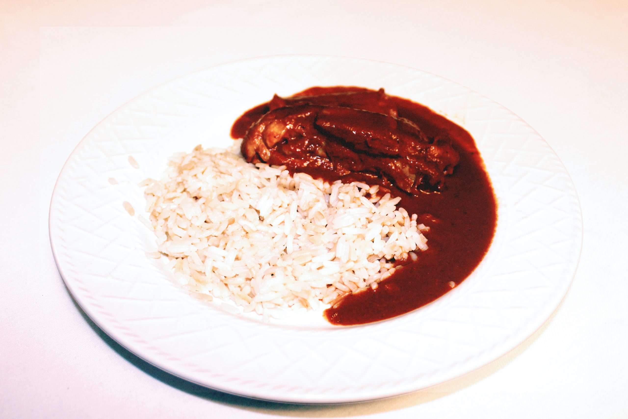 A white dish with half rice and half dark chocolate colored meat stew next to the rice.