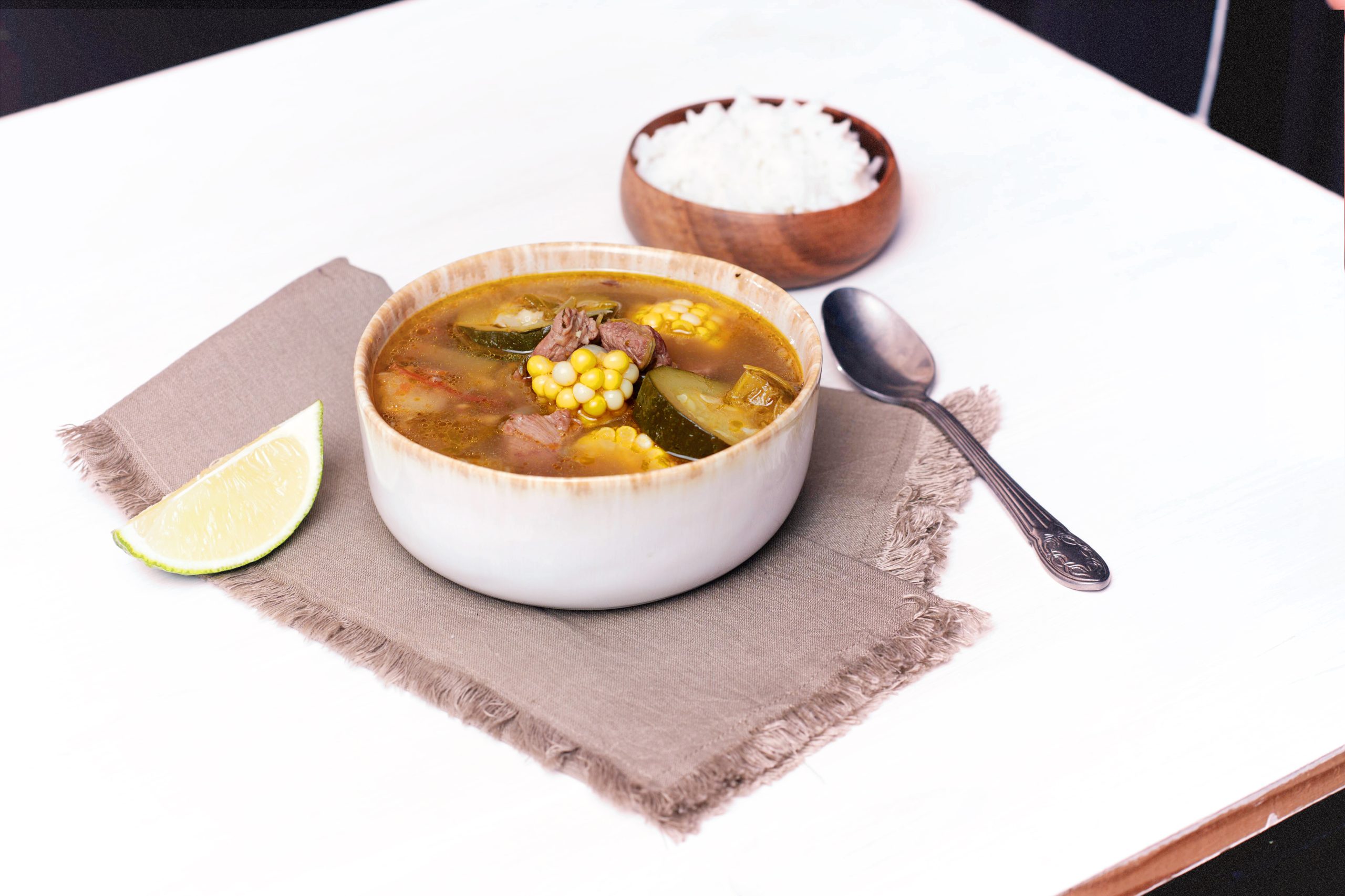 A beautiful soup with corn and other vegetables is on display on a white table.