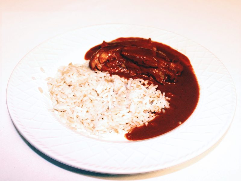 A white dish with half rice and half dark chocolate colored meat stew next to the rice.