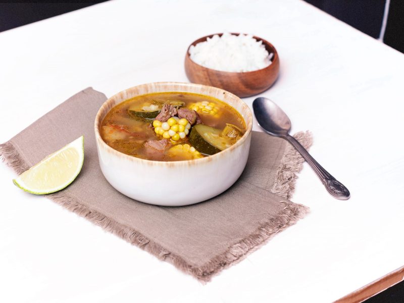 A beautiful soup with corn and other vegetables is on display on a white table.