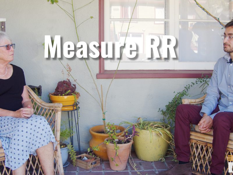 A woman with short grey hair sits on a porch talking to a young Latino man.