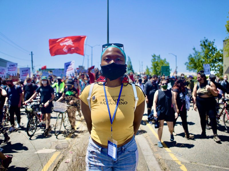 An image of an African American woman with short, blue hair standing in front of a group of marchers during a Juneteenth event.