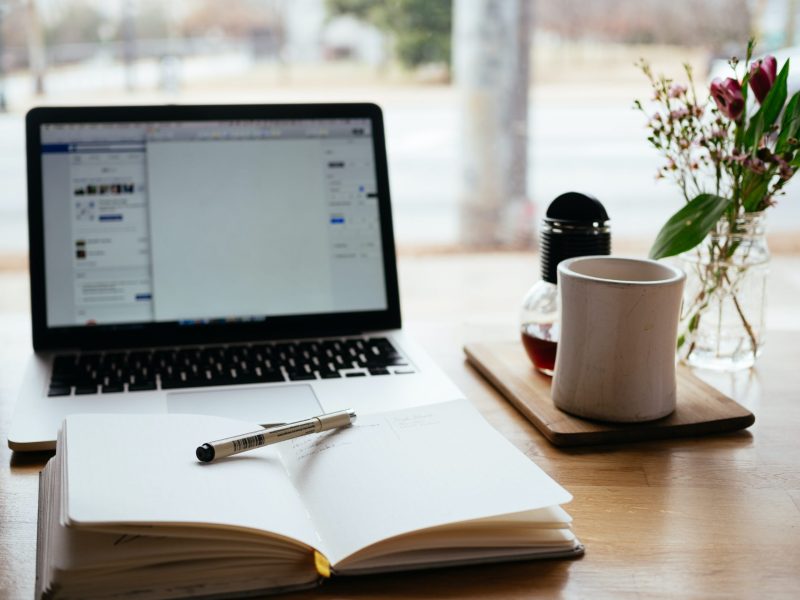 An image of a laptop and notebook with a coffee mug