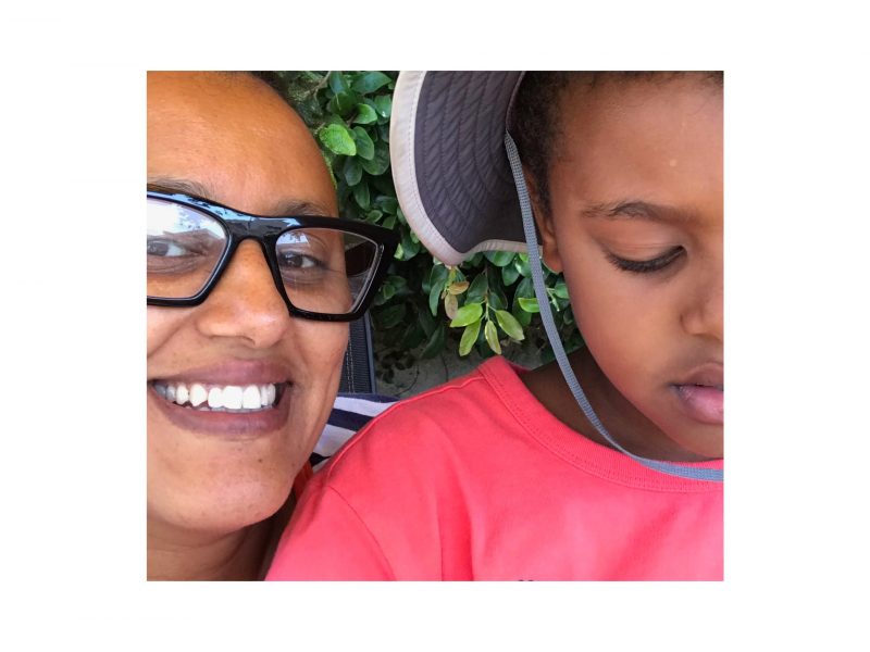 An African American woman with glasses is smiling, next to a young boy wearing a hat.