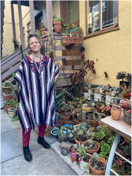 A woman wearing a poncho stands outside a building and smiles