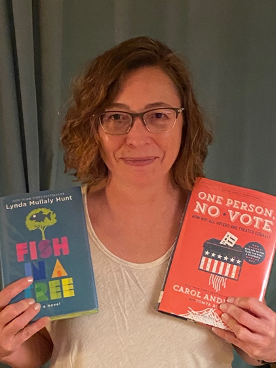 An image of a woman wearing glasses and holding two books.