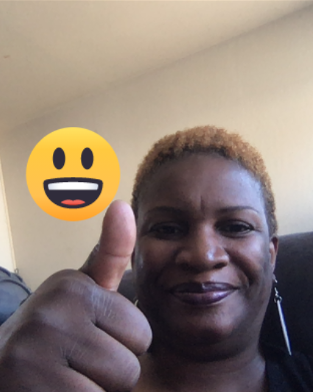 An African American woman with short hair smiles at camera with her thumbs up and a smile emoji on the screen.