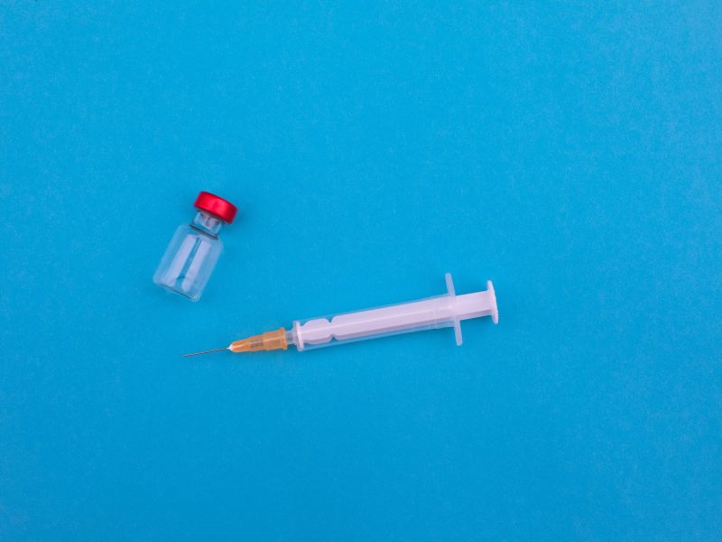 image of a vial and needle against a blue background