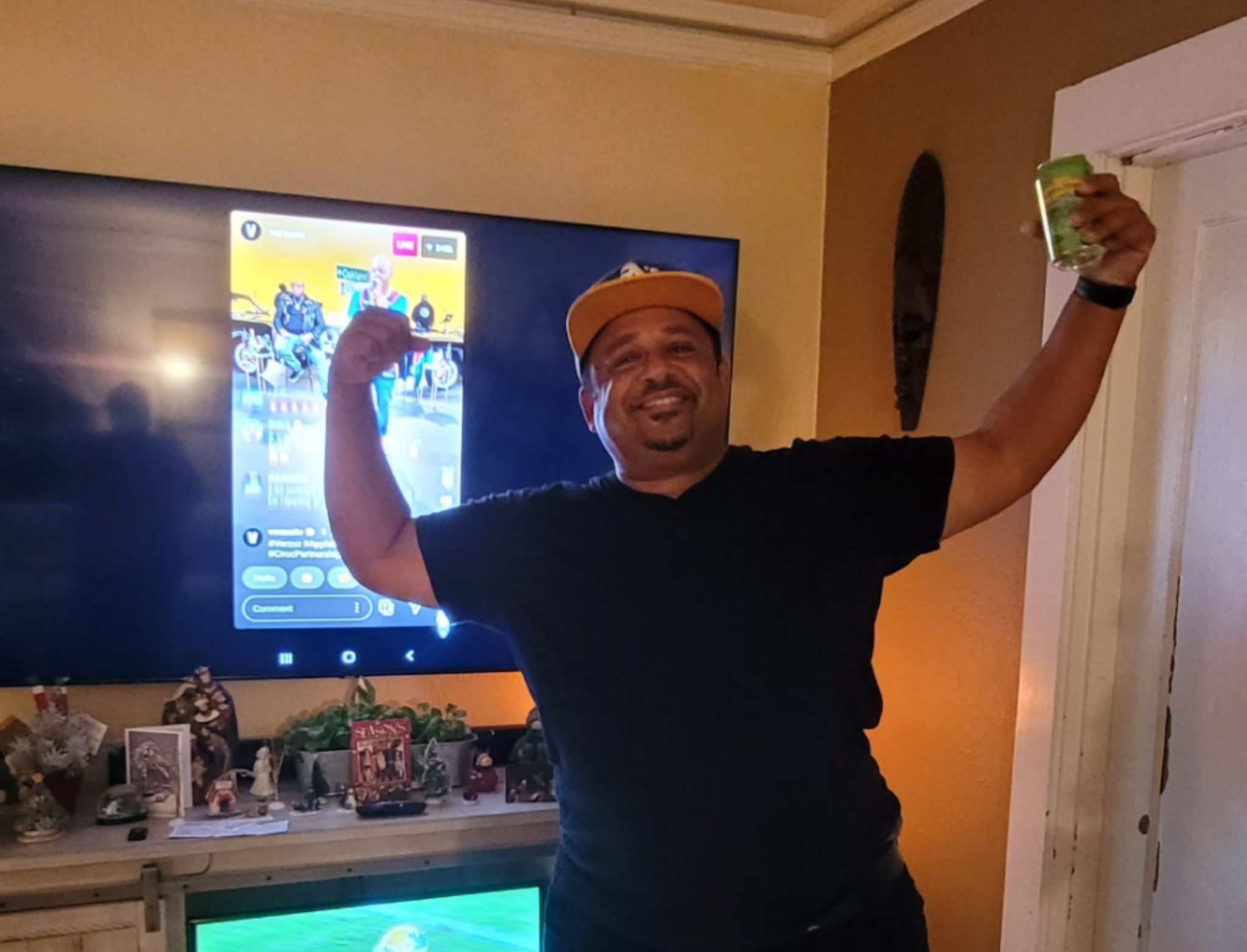 An image of a man wearing a baseball cap holding his arms up in triumph in front of a TV.