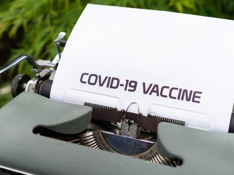 A typewriter with a paper that says "COVID-19 VACCINE"