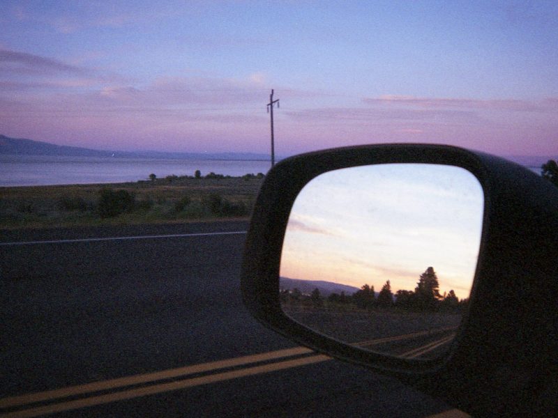 An image at dusk of a rearview mirror and pretty pink clouds.