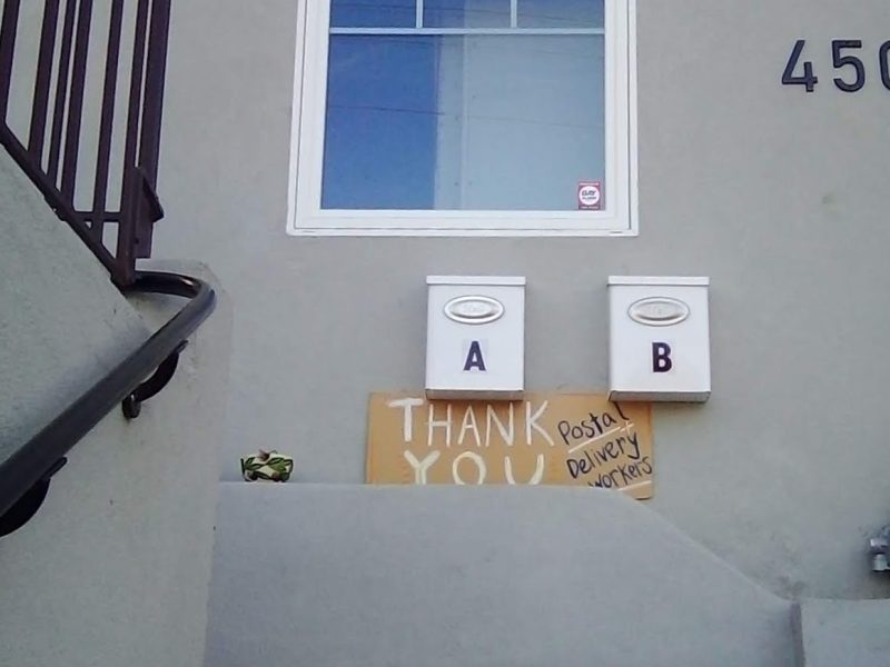 a grey stone house with a handwritten cardboard sign thanking postal workers