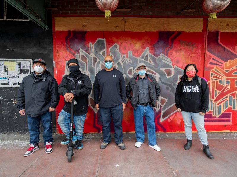A diverse group of Asian Americans stand in front of a bright mural in Chinatown