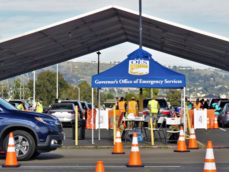 Orange cones line the way in a parking lot at the Oakland Coliseum, where military dressed people point the way. A big blue tent that says "Governor's Office of Emergency Services" is set up.