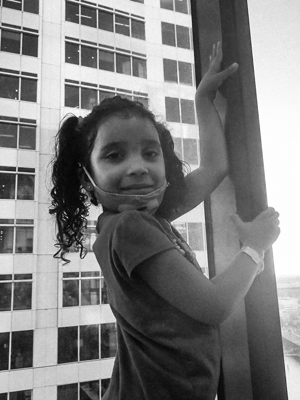 a black and white photo of girl in curly pigtails in front of big hotel window