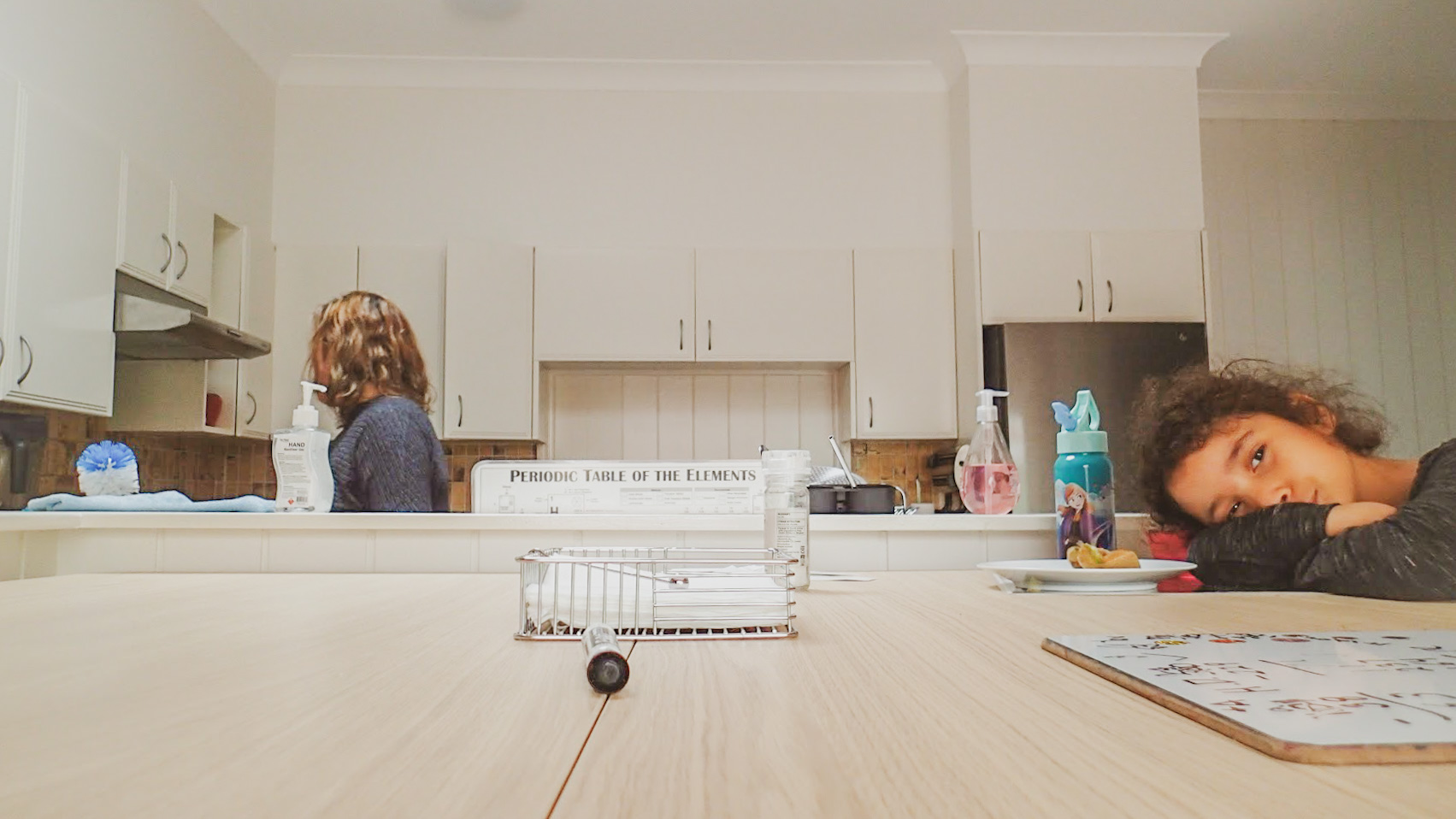 a soft image of five year old laying her head on the kitchen table while her stepmom is in the background