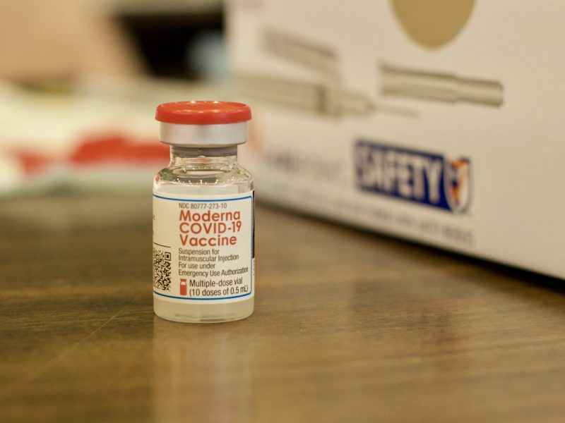 close up of a small vial of COVID vaccine with a red cap.