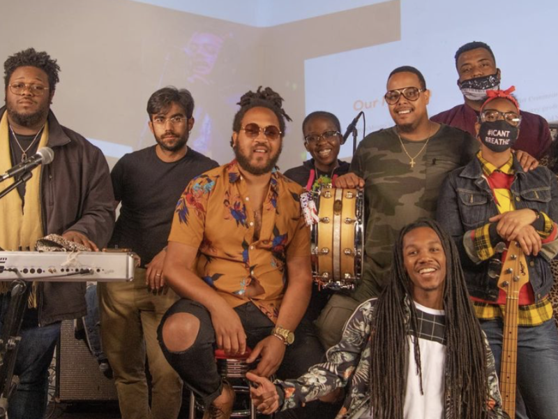 A group of Black and African American people standing near keyboard and other instruments in a band.