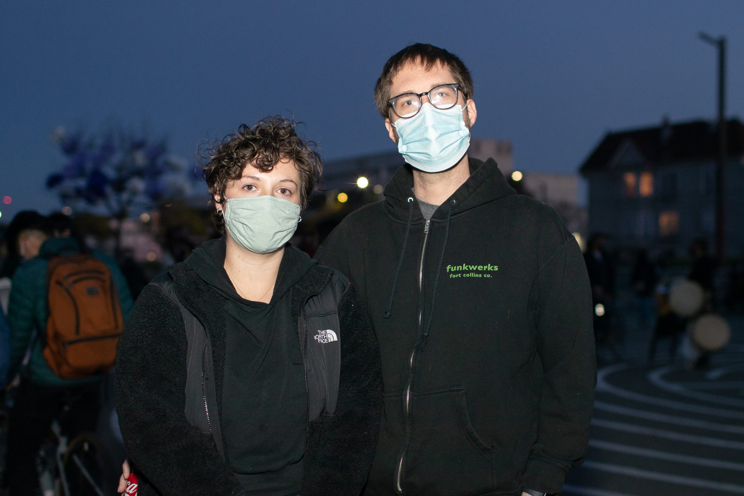 A white woman and white man wearing surgical masks pose for photo in the evening at Madison Park in Oakland.