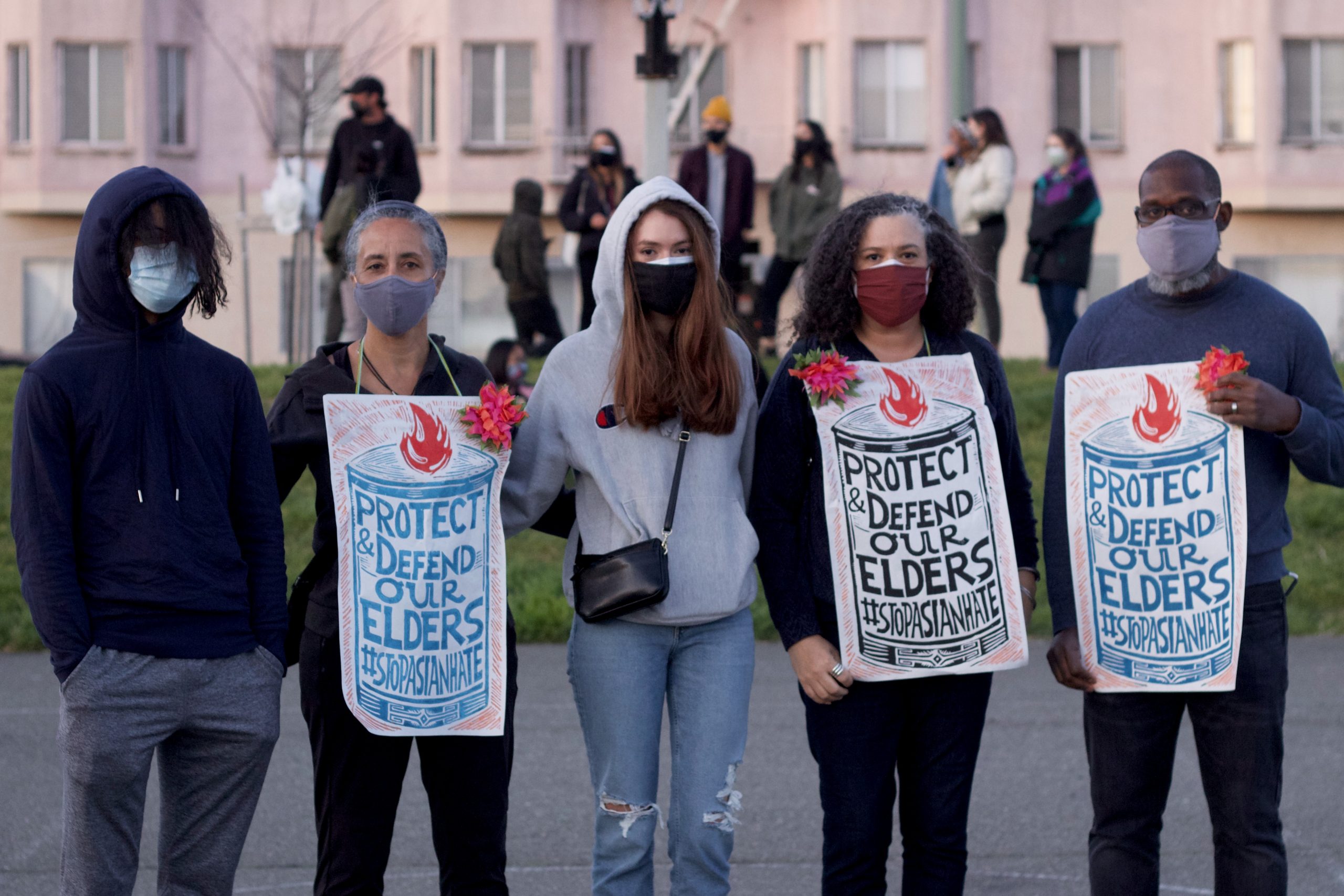 A multiracial family of five stands with signs that say "Protect & Defend Our Elders #StopAsianHate"